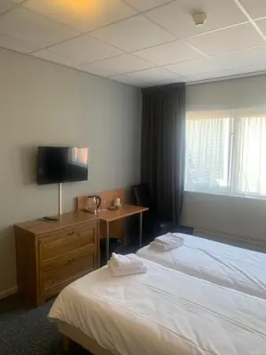 a hotel room with two beds and a desk and a television at Hotel Flevo in Zeewolde