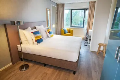 a bedroom with a bed with white sheets and pillows at Amrâth Apart-Hotel Schiphol Badhoevedorp in Badhoevedorp