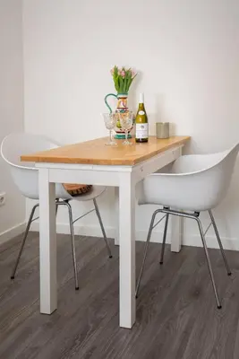 a white dining table and two chairs with wine bottles and flowers at Casita del Pueblo in Zandvoort