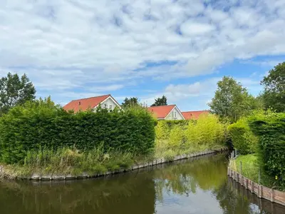 a river with bushes and houses in the background at Holiday Home Stern Comfort-2 by Interhome in Noordwijk