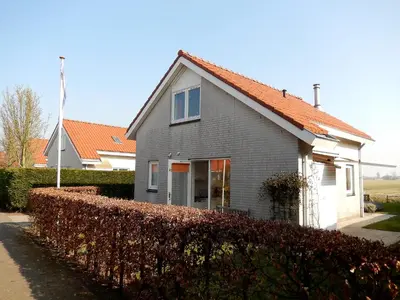 a gray house with an orange roof next to a hedge at Holiday Home Stern Comfort-2 by Interhome in Noordwijk