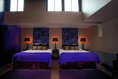 a bedroom with two beds with purple sheets and windows at Hotel Sebastians in Amsterdam