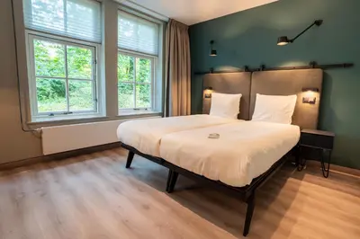 a large bed in a room with two windows at Hotel Kontakt der Kontinenten in Soesterberg