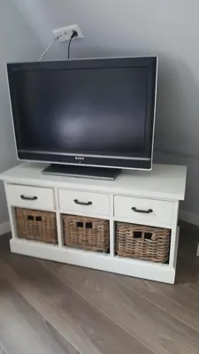 a tv on top of a white tv stand with baskets at Het Zwanennest in Den Ilp