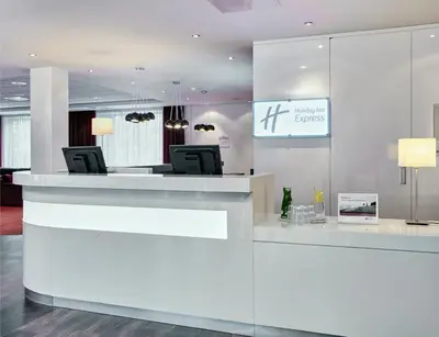 a white lobby with a reception desk with chairs at Holiday Inn Express Amsterdam - Schiphol by IHG in Hoofddorp