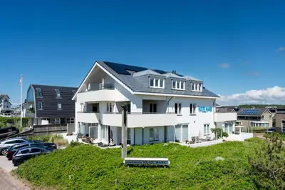 a large white house with cars parked in a parking lot at Huize Mare Appartementen in Bergen aan Zee