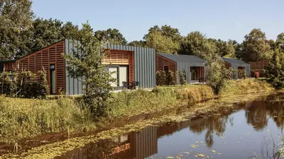 a house on the riverbank with a view of it at Dutchen Suitelodges Gooilanden in Loosdrecht