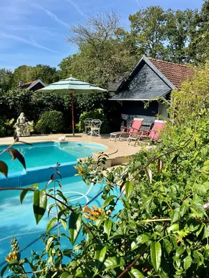 a swimming pool with an umbrella and chairs and a house at The Pool House in Den Dolder