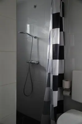 a bathroom with a shower with a black and white shower curtain at budget rooms Doppenberg in Zandvoort