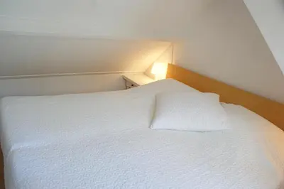 a bedroom with a white bed with a white pillow at Egmond aan Zee Vakantiehuisje in Egmond aan Zee