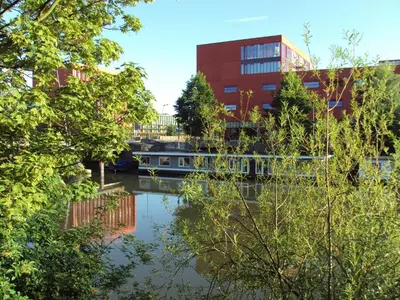 a river in front of a building with a boat at Boathotel in Amsterdam