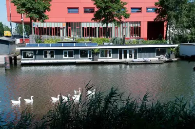 a boat on a river with swans in front of a building at Boathotel in Amsterdam