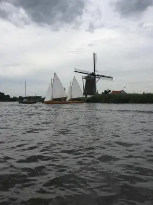 three boats with white sails on the water with a windmill at Groeten uit Hoogmade - rural cottage in Hoogmaden