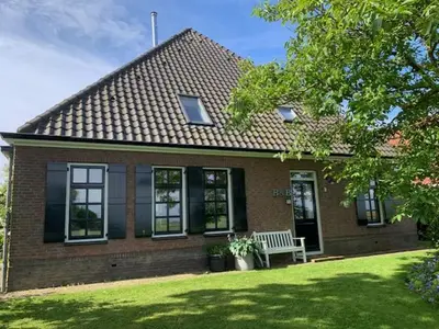 a brick house with a bench in the front yard at Gastenverblijf Eenigenburg in Eenigenburg