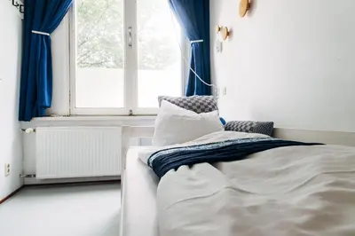 a bedroom with a bed with blue curtains and a window at ClinkCoco in Amsterdam
