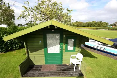 a small house with a green door and a white chair at Camping Recreatiepark Aalsmeer in Aalsmeer