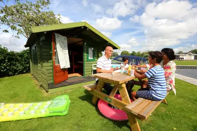 a group of people sitting at a picnic table outside a play house at Camping Recreatiepark Aalsmeer in Aalsmeer