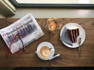 a table with a piece of cake and a cup of coffee and a newspaper at Slapen bij hofman in Alkmaar