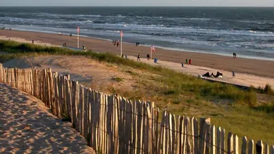 a fence on the beach with people walking on the beach at Sea Star Egmond aan Zee in Egmond aan Zee