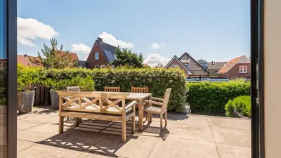a wooden table and bench on a patio with houses at Goudkust 3 'At Sea' in Bergen