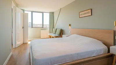 a bedroom with a large white bed and a chair at Goudkust 3 'At Sea' in Bergen