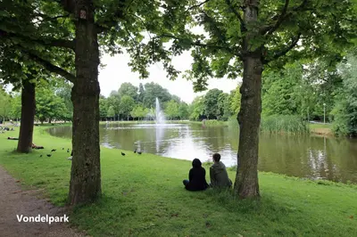two people sitting on the grass in front of a pond at Vondelpark Suite in Amsterdam