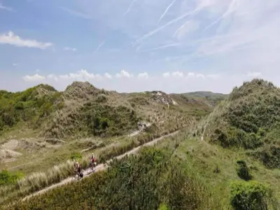a group of people walking down a dirt road on a hill at Holiday Home Bergen aan Zee near Beach in Bergen aan Zee