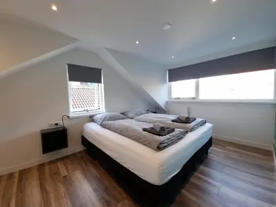 a bedroom with a large bed and two windows at Zomerhuis de Jong in Egmond aan Zee