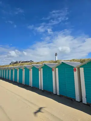 a row of blue beach huts on a beach with a lighthouse at Zomerhuis de Jong in Egmond aan Zee