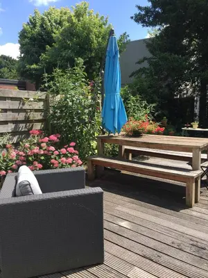 a patio with a table and a blue umbrella and a bench at De Vuurdoorn in Bergen
