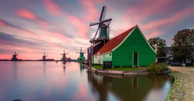 a green barn with a windmill in the water at Huisje Britt met grote tuin en veel privacy in Dirkshorn