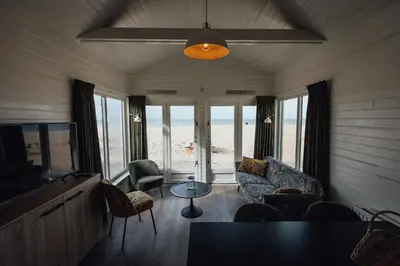 a living room with a couch and chairs and the beach at Logeren aan Zee in Katwijk aan Zee