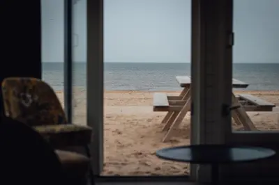 a room with a view of the beach with a chair and a table at Logeren aan Zee in Katwijk aan Zee