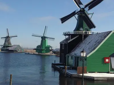a group of windmills on the water next to a building at Stay overnight at Windmill Village Zaanse Schans - Amsterdam in Zaandam