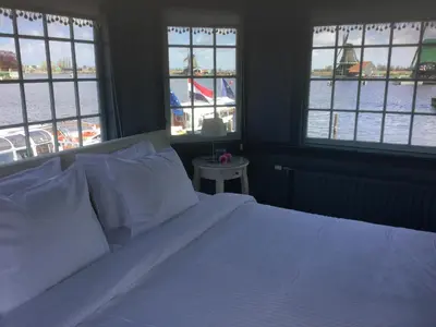 a bedroom with a bed with white sheets and windows at Stay overnight at Windmill Village Zaanse Schans - Amsterdam in Zaandam