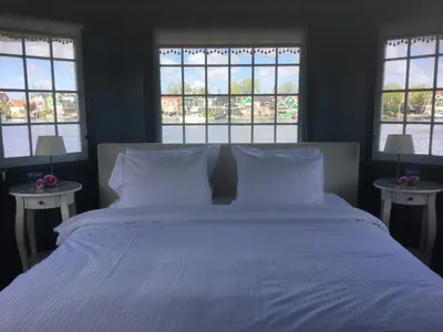 a bedroom with a large bed with white sheets and windows at Stay overnight at Windmill Village Zaanse Schans - Amsterdam in Zaandam