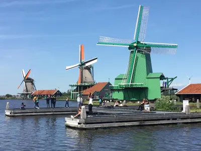a group of windmills with people on a dock in the water at Stay overnight at Windmill Village Zaanse Schans - Amsterdam in Zaandam