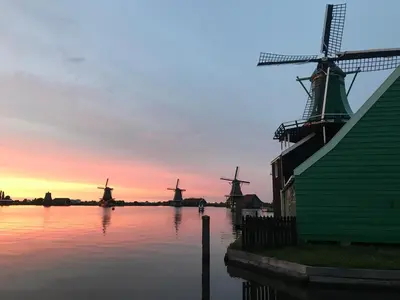 a group of windmills on a river with a sunset at Stay overnight at Windmill Village Zaanse Schans - Amsterdam in Zaandam