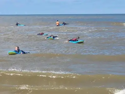 a group of people laying on surfboards in the ocean at Holiday Home Bergen near Beach & Dunes in Bergen aan Zee