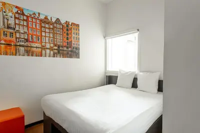 a bedroom with a white bed with a painting on the wall at easyHotel Amsterdam City Centre South in Amsterdam