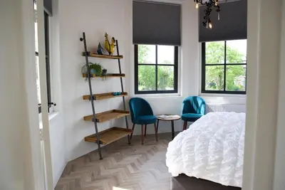 a bedroom with two chairs and a bed and windows at Het Torentje aan de IJssel in Montfoort