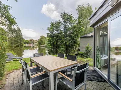 a wooden table and chairs on a patio with a lake at Center Parcs De Eemhof in Zeewolde