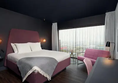 a bedroom with a large bed and a pink chair at Van der Valk Hotel Amsterdam - Amstel in Amsterdam