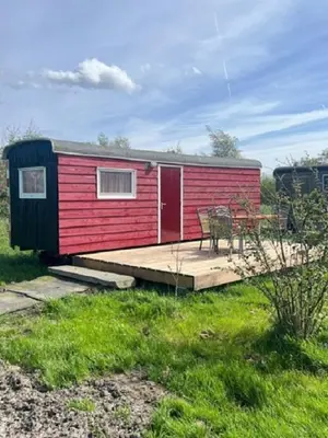 a red and black tiny house with a wooden deck at Bed & Breakfast ARKEN AE in Zuiderwoude