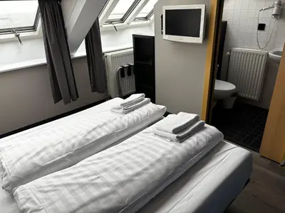 two beds in a room with a tv and a bathroom at Hotel Oostereiland in Hoorn