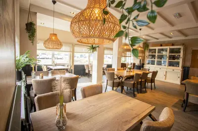 a restaurant with wooden tables and chairs and lights at Hotel De Boei in Egmond aan Zee