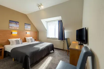 a hotel room with a bed and a flat screen tv at Hotel De Boei in Egmond aan Zee