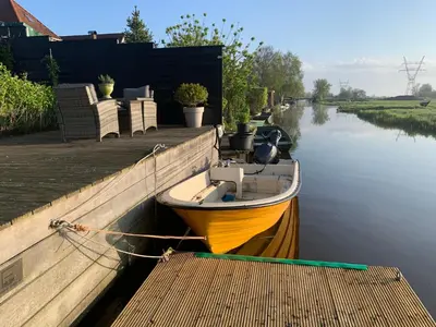 a small boat tied to a dock on a river at Paleis Noordeinde in Grootschermer