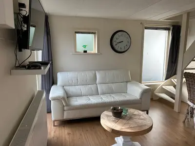 a living room with a white couch and a clock on the wall at Appartement Zandwerven 23 in Spanbroek