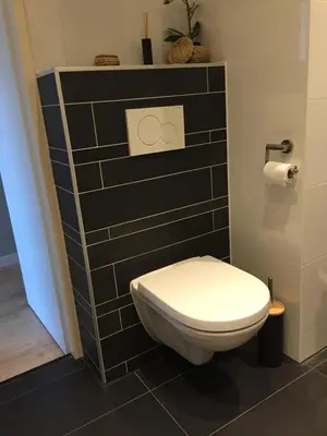 a toilet in a bathroom with a black tile wall at Zeesterflat 117 in Egmond aan Zee